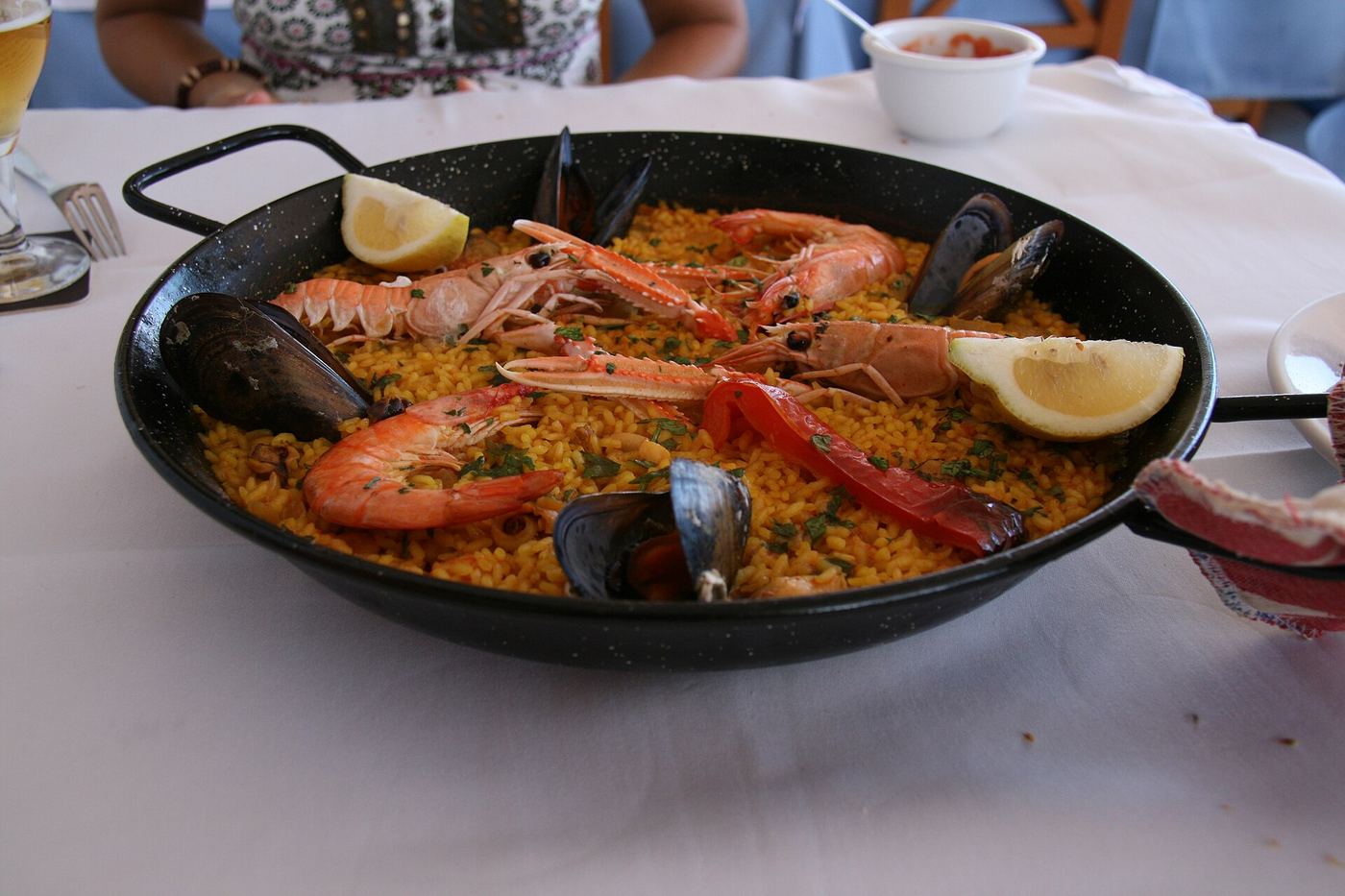 Una paella con gamberoni, cozze e spicchi di limone, in padella su un tavolo apparecchiato
